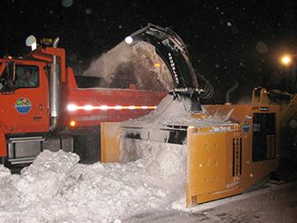 equipment blowing snow into a dump truck for removal
